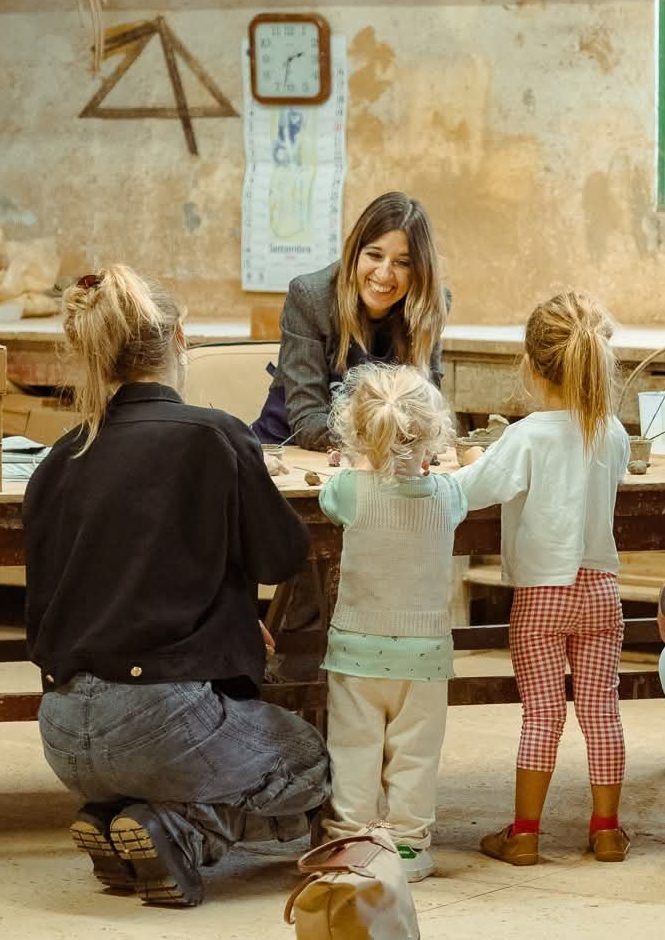 Chiara sorridente al tavolo con due bambine che modellano l’argilla, alla Fornace Curti